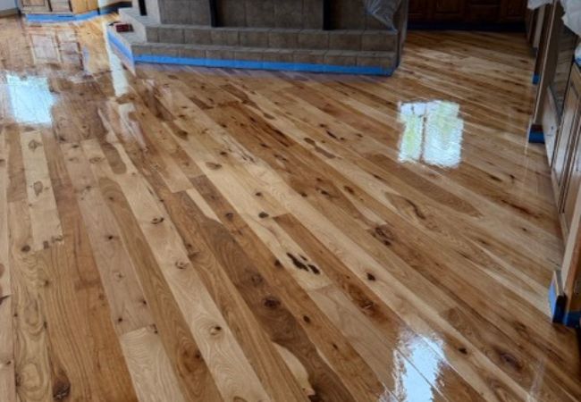 Refinished knotty hardwood floor with a high-gloss finish beside a stone hearth